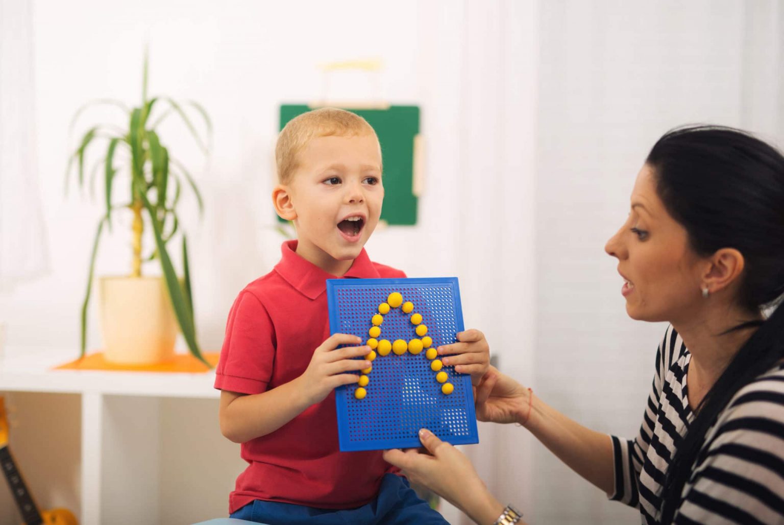A young boy holding a sign with an A on it learning how to say A in speech therapy.